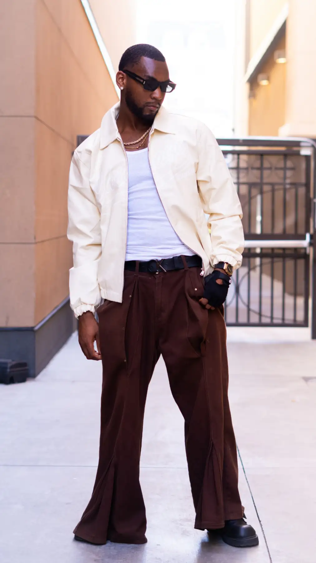 Bren Got Hits standing in a sunlit alley in a cream Chicago jacket and wide brown trousers