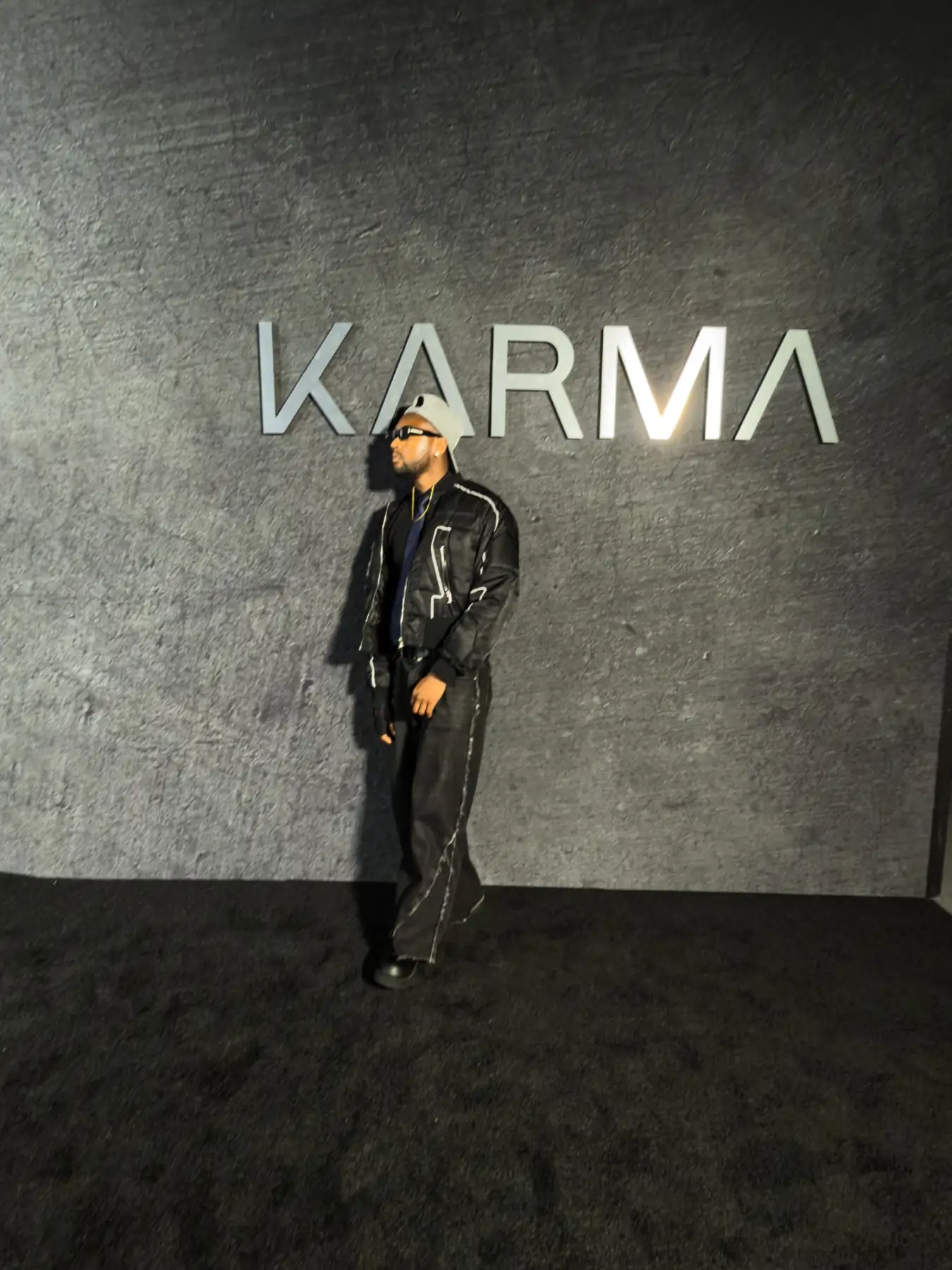 Bren Got Hits in black with a grey cap and sunglasses in front of the KARMA wall