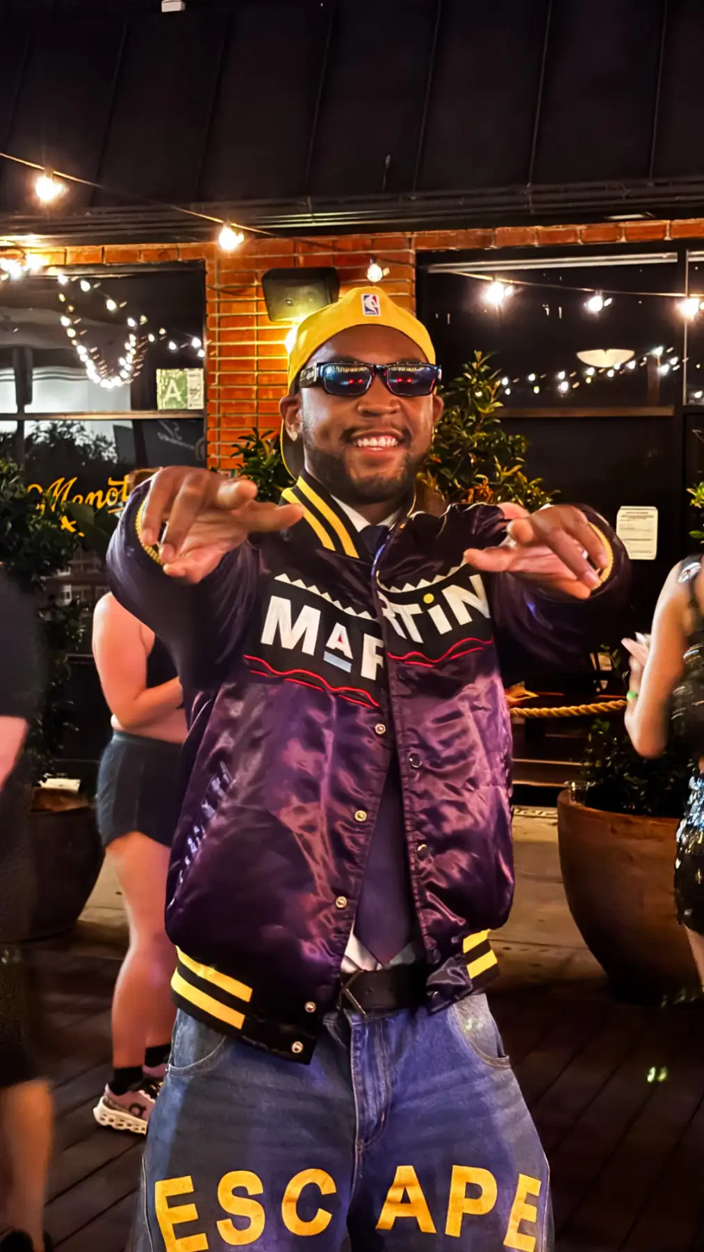 Bren Got Hits smiling in a purple Martin satin jacket and yellow cap